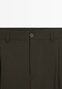 Ciemnozielona talia spodni z zapięciem na guzik, szlufkami na pasek i przeszyciami na przednim szwie na gładkim materiale.