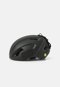 Casque de vélo noir avec un design aérodynamique, plusieurs aérations, une surface texturée et une sangle sécurisée. Présente un logo réfléchissant et une étiquette MIPS.