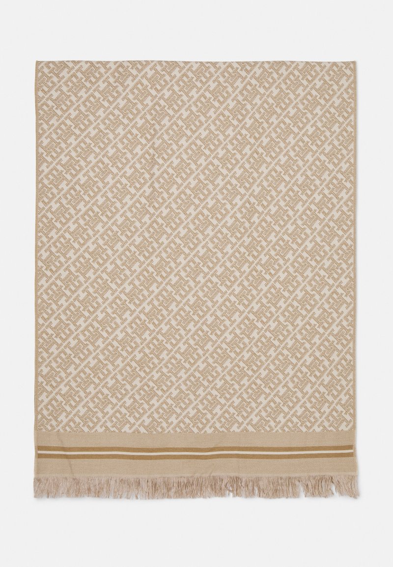 Coperta intrecciata beige con motivi geometrici, dotata di una frangia decorativa e strisce orizzontali nella parte inferiore di una tonalità leggermente più scura.