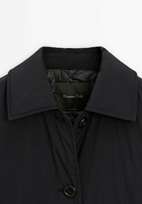 Veste noire boutonnée avec col large, doublure matelassée et étiquette de vêtement cousue à l'intérieur du col.