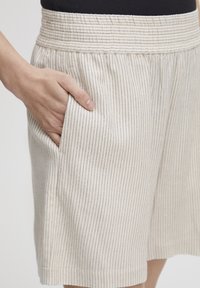Pantalones cortos de rayas beige con cinturilla elástica y bolsillo lateral, que cuentan con finas rayas verticales en azul marino y una tela suave y ligera.