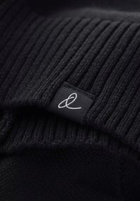 Tessuto a maglia nera con texture a coste e una piccola etichetta nera con dettagli in cucitura bianca a carattere corsivo "&".