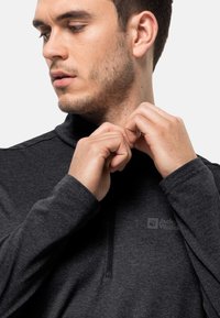 Schwarzer Zip-Fleece-Pullover mit langen Ärmeln und hohem Kragen. Markenlogo auf der Brust. Modell passt den Kragen an, strukturiert sichtbarer Stoff.