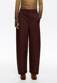 Laiene püksid sügavas burgundi värvi kangas. Omavad kõrget taljet ja küljetaskuid, sobitatud pruunide nahast ankle saapadega.