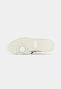 White rubber sole with herringbone pattern, a circular design element, and a rectangular patch. Smooth texture, sturdy construction.