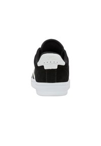 Zapatilla de ante negra con acentos blancos, que presenta una puntera redondeada, suela blanca plana y un panel trasero texturizado con logo en relieve.