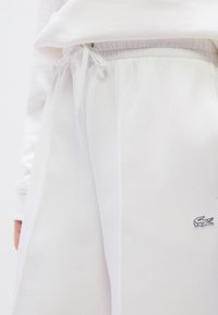 Λευκό βαμβακερό παντελόνι φόρμας με κορδόνι στη μέση, με διακριτή υφή και μικρό κεντητό λογότυπο στο πόδι.