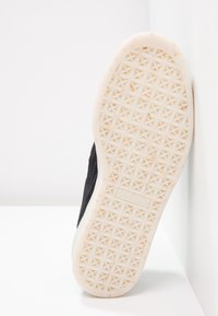 Baskets noires avec une tige en tissu texturé et une semelle en caoutchouc blanche ornée d'un motif étoile. Logo visible sur la semelle.