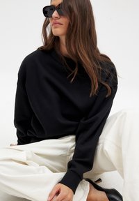 Czarny, oversize bluza z prążkowanymi mankietami, w zestawieniu z kremowymi, szerokimi spodniami i czarnymi szpilkami. Gładki materiał o luźnym kroju.
