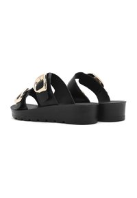 Sandalias negras con tiras anchas y grandes hebillas metálicas, con una suela gruesa texturizada que presenta un ligero alzamiento y detalles en zigzag.