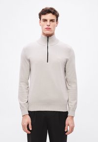 Helehall triiksärk kõrge krae ja veerandlõhikutega, millel on väike logomärk rinnal ning soonikkoes mansetid ja alumine serv.