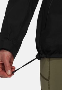 Svart lättviktig jacka med texturerad tyg. Handdraget justerbart snöre i midjan, ihop med olivgröna leggings med sömdetaljer.