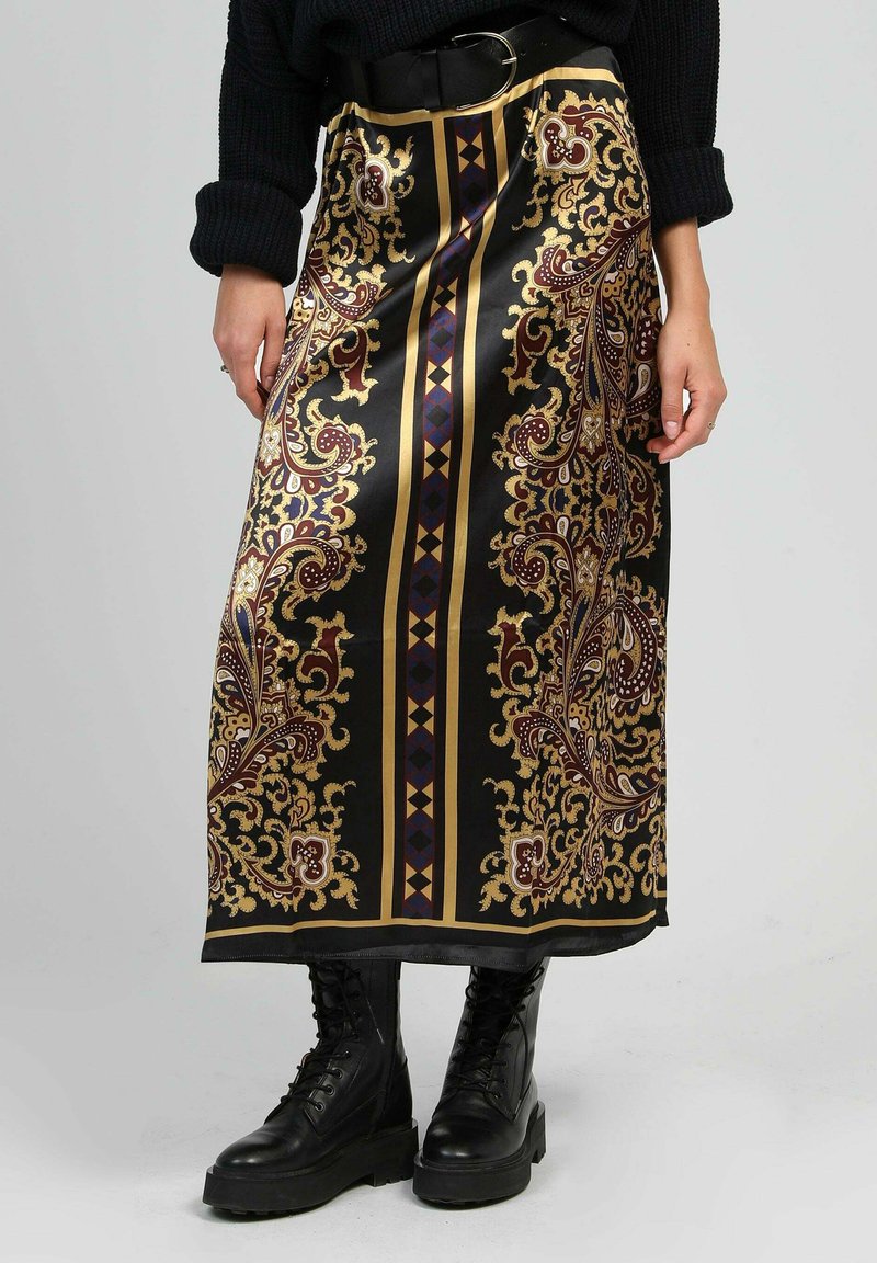 Jupe en satin noir avec des motifs paisley dorés et bordeaux, agrémentée de rayures géométriques. Portée avec des bottes de combat noires.