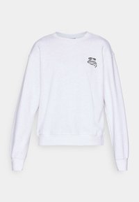 Sweatshirt blanc à manches longues et col rond, avec un petit graphique noir et un texte sur la poitrine gauche lisant "Karma" avec des yeux stylisés.