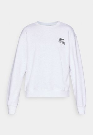 Sweatshirt blanc à manches longues et col rond, avec un petit graphique noir et un texte sur la poitrine gauche lisant "Karma" avec des yeux stylisés.