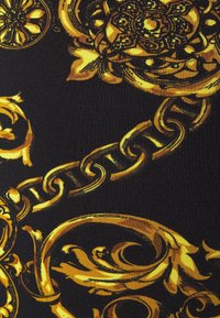 Auf schwarzem strukturiertem Stoffhintergrund befindet sich ein komplexes Muster aus barockstiligen goldenen Ketten und floralen Ranken.