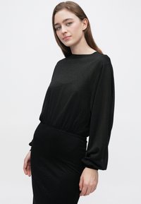 Černé šaty s přiléhavým pasem, dlouhými rukávy a měkkou, lesklou texturou. Design zahrnuje lodičkový výstřih a elastické detaily.