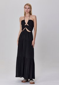 Robe maxi noire avec un design de col halter, des découpes à la taille et une texture de tissu superposée. Présente une silhouette fluide.