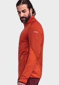 Men's orange fleece jacket with a high collar, textured fabric, and side pockets. Features a logo on the shoulder and a fitted design.