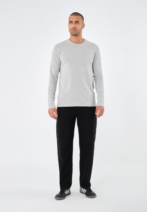 Grijze langwerpige t-shirt in een zachte stof, gecombineerd met zwarte ruime broek en zwarte sneakers met witte strepen.