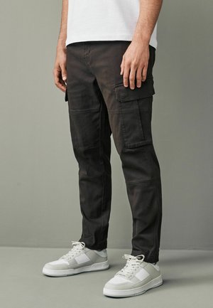 Svarta cargobyxor med flera fickor, en slim fit och subtila sömnadsdetaljer, matchade med vita sportskor.