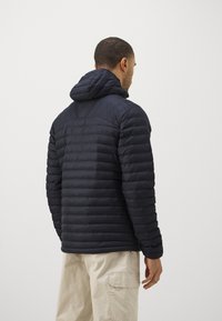 Tengerés kék pufiklódzseki kapucnival, steppelt designnal és bordázott textúrával. Fitted siluettal rendelkezik, és világos színű nadrágok fölött viselik.