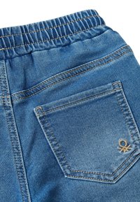 Džínové kalhoty s elastickým páskem, středně modré barvy, s jednou zadní kapsou na přišitý štítek a béžovým vyšitým logem.