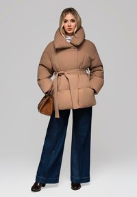 Tan pufferjakke med stor krave, bælte i taljen og quiltet tekstur. Parret med mørke flare jeans og sorte hæl støvler.