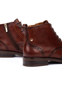 Bottines en cuir marron avec des détails en brogue, dotées d'une fermeture éclair sur le côté, d'un bout rond et d'un talon en bois bas.