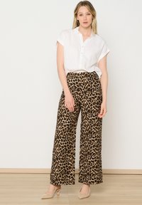 Witte kortekrans knoopshirt gecombineerd met een wijde leopardprint broek in tan en zwart. Het model draagt ook nude hakken.