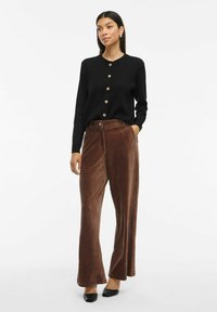 Cardigan noir avec des boutons dorés, associé à un pantalon en velours côtelé marron à jambes larges. Texture lisse, coupe décontractée et rayures verticales bien définies.