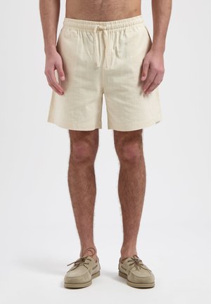Beige linnen shorts met een elastische tailleband en trekkoord, voorzien van een gestructureerd oppervlak en zijzakken, gecombineerd met lichte schoenen.