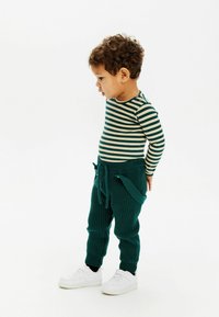 Randig långärmad topp i grön och beige, kombinerad med ribbade tealbyxor med snörning. Skorna är vita sneakers.