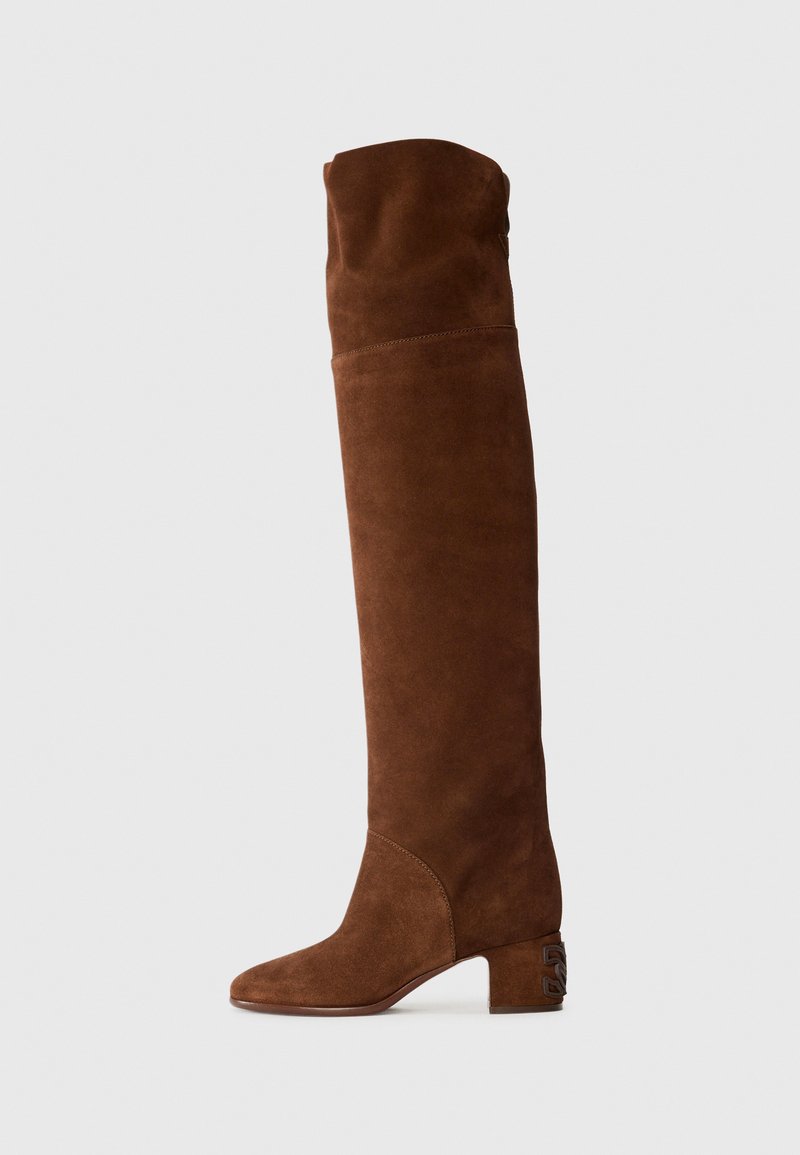 Botas de ante marrón hasta la rodilla con punta afilada y un bajo tacón cuadrado, que presentan un acento de hardware único en el costado del tacón.