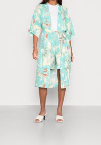 Jasnoniebieskie kimono z kolorowymi wzorami paisley, z szerokimi rękawami i paskiem w talii, zestawione z białymi sandałami na obcasie.