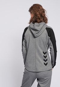 Hoodie gris avec des accents noirs, doté d'une capuche, d'une coupe ajustée et d'un motif en chevron au dos. Fabriqué à partir d'un tissu doux et texturé.