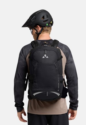 Zaino nero con tessuto testurizzato e molteplici scomparti, indossato con un casco nero. Presenta dettagli riflettenti e spallacci regolabili.