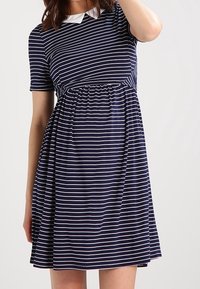 Kvinna iklädd en marinblå klänning med vita horisontella ränder och korta ärmar, med en rynkad midja och en vit krage.