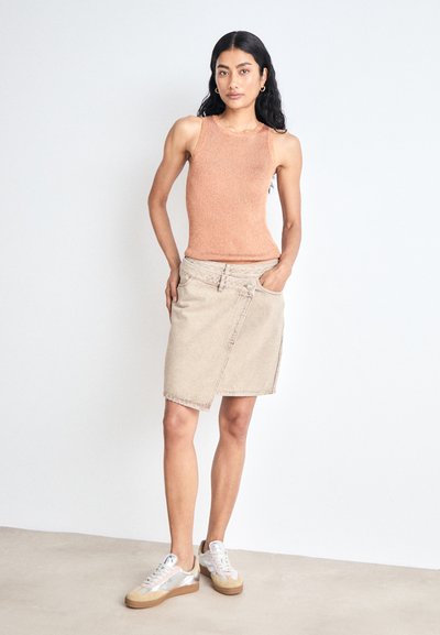 Débardeur côtelé pêche associé à une jupe enveloppante beige clair. La tenue est complétée par des baskets avec un accent argent métallique.