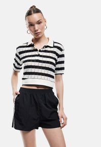 T-shirt polo tricot à rayures noires et blanches à manches courtes avec un col, associé à un short noir ample avec poches latérales.