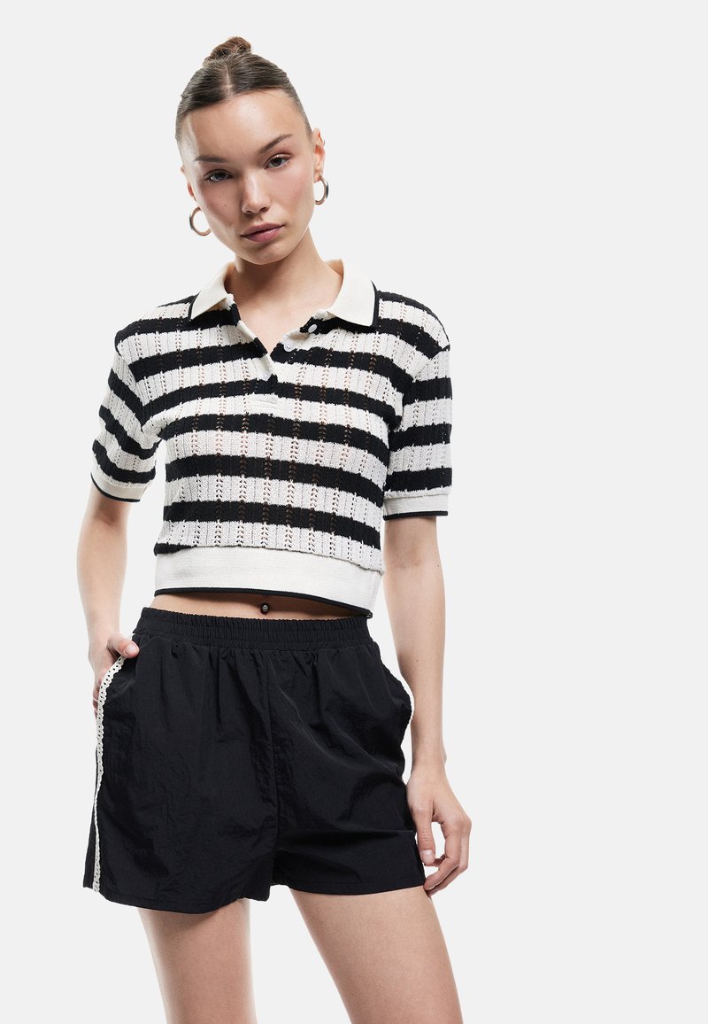 T-shirt polo tricot à rayures noires et blanches à manches courtes avec un col, associé à un short noir ample avec poches latérales.