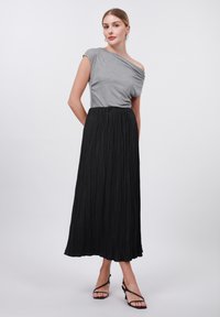 Top grigio senza spalline, gonna maxi nera plissettata e tacchi neri con cinturini. Texture morbide, design fluido e modelli stratificati visibili.