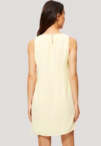 Vestido sin mangas amarillo, tejido ligero, cuello alto, detalle de abertura en la espalda, textura suave, que cae justo por encima de las rodillas, corte recto.