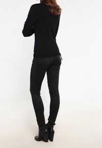 Pull noir ajusté à manches longues associé à un jean skinny noir. La tenue est complétée par des bottines noires à talon épais.