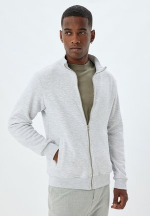 Sweatshirt zippé gris clair en tissu doux, doté d'un col montant, de poches latérales et de poignets et d'un ourlet côtelés.