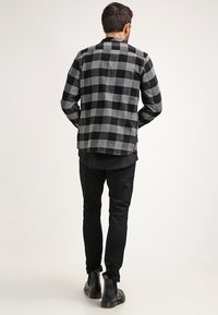 Camisa de franela a cuadros en negro y gris, diseño abotonado, textura suave, llevada sobre una camiseta negra en capas, combinada con jeans negros y botas.