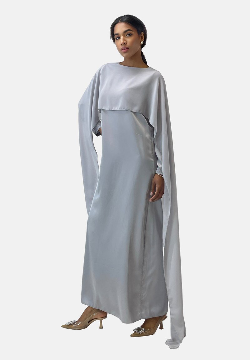 Robe en satin gris clair avec des manches longues et une silhouette fluide. Elle présente un col haut et des manches superposées en forme de cape.