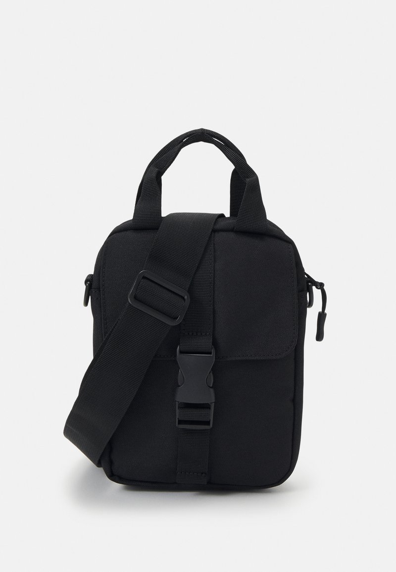 Black fabric crossbody bag with adjustable strap, dual top handles, front flap, zip closure, and a smooth texture. Simple rectangular shape.