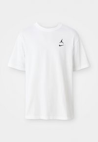 T-shirt en coton blanc avec un col rond, des manches courtes et deux petits logos noirs : le Jumpman et le swoosh de Nike sur le côté gauche de la poitrine.