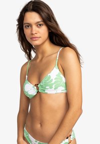 Groen en witte bikini-top met grote bladerenpatronen, driehoekige cups en een centrale ringaccent. Verstelbare banden maken het ontwerp af.
